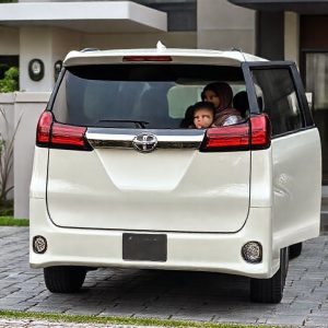 Toyota Voxy bekas berwarna putih atau hitam sedang terparkir elegan di depan rumah modern dengan pintu geser terbuka. Terlihat keluarga muda dengan dua anak kecil keluar dari mobil, menunjukkan kemudahan akses.