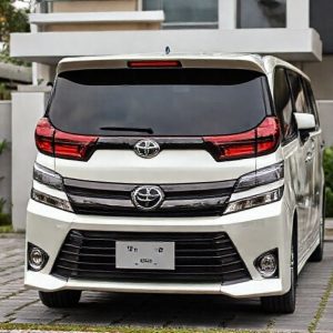 Toyota Voxy bekas berwarna putih atau hitam sedang terparkir di depan rumah modern dengan anggota keluarga (ayah, ibu, 2 anak) tersenyum di dekatnya.